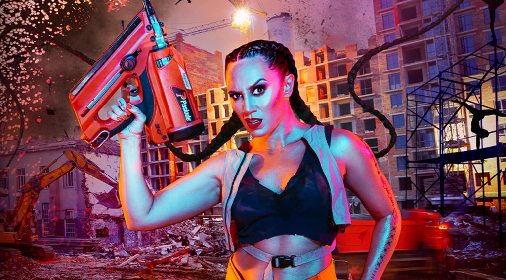 Lisa Fa’alafi wears hi-vis gear and holds a nail gun in front of a demolition site.